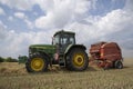 A tractor uses a trailed bale machine to collect straw in the field and make round large bales. Agricultural work, baling, baler,
