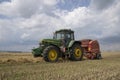 A tractor uses a trailed bale machine to collect straw in the field and make round large bales. Agricultural work, baling, baler,