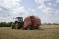 A tractor uses a trailed bale machine to collect straw in the field and make round large bales. Agricultural work, baling, baler,