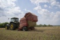 A tractor uses a trailed bale machine to collect straw in the field and make round large bales. Agricultural work, baling, baler,