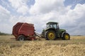 A tractor uses a trailed bale machine to collect straw in the field and make round large bales. Agricultural work, baling, baler,