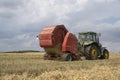 A tractor uses a trailed bale machine to collect straw in the field and make round large bales. Agricultural work, baling, baler,