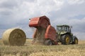 A tractor uses a trailed bale machine to collect straw in the field and make round large bales. Agricultural work, baling, baler,