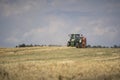 A tractor uses a trailed bale machine to collect straw in the field and make round large bales. Agricultural work, baling, baler,