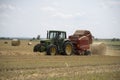 A tractor uses a trailed bale machine to collect straw in the field and make round large bales. Agricultural work, baling, baler,