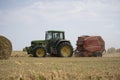 A tractor uses a trailed bale machine to collect straw in the field and make round large bales.