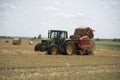 A tractor uses a trailed bale machine to collect straw in the field and make round large bales.