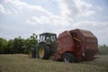 A tractor uses a trailed bale machine to collect straw in the field and make round large bales.