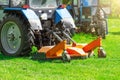 Tractor uses trailed lawn mower to mow grass on city lawns, back view