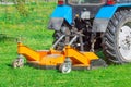 Tractor uses trailed lawn mower to mow grass on city lawns, back view Royalty Free Stock Photo