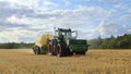 Tractor using a baler in a field, with the baler depositing a bail of straw onto the ground. UK