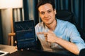 Trader in casual looking at camera stock with pointing laptop. Pecuniary.
