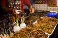 Trader of fried insects, grasshoppers and larvae on street food market selling exotic asian snacks