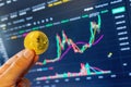 Trader holding bitcoin in front of computer screen showing price chart