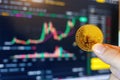Trader holding bitcoin in front of trading screen showing price chart