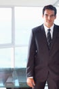 Man in dark suit wearing striped tie standing right by glass table and windows, copy space Royalty Free Stock Photo