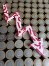 arrow down formed with plasticine in red and white and stacked coins of mexican pesos