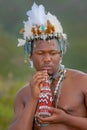 A Traditional African Dressed male with a beaded headdress drink from a beaded bottle.