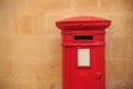 Traditional, British postbox in red color. Mailbox that receives the letters. Light orange limestone wall for background. Copyspac