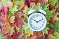 Traditional alarm clock on a background of green, yellow, orange, and red maple leaves, fall time change concept Royalty Free Stock Photo