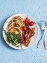 Traditional american breakfast - crispy bacon, pancakes with maple syrup, roasted tomatoes, arugula. On a blue background