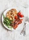 Traditional american breakfast - crispy bacon, pancakes with maple syrup, roasted tomatoes, arugula. On a light background