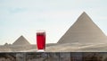 Traditional Arab herbal tea karkade in a glass against background of Great Pyramids of Chephren Khafra and Cheops Khufu in Giza. Royalty Free Stock Photo