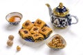 Traditional arabic dessert baklava with cashew, walnuts, raisins on plate, bowl, teapot with Uzbek national ornament on white wood
