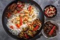 Traditional Asian food - rice noodles with seafood, salad, red pepper and fried mushrooms are on a gray table. Royalty Free Stock Photo