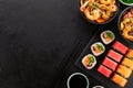 Wok noodles with shrimps and vegetables in a black bowl, sushi roll and seaweed salad on a black slate background Royalty Free Stock Photo