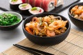 Traditional Asian food set. Wok noodles with shrimps and vegetables in a black bowl, sushi roll and seaweed salad Royalty Free Stock Photo