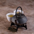 Traditional Asian herbal tea, cooked in a cast-iron kettle with dry herbs and two tea bowls on a textured background. Close-up