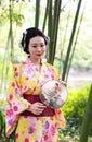 Traditional Asian Japanese beautiful Geisha woman wears kimono hold a fan on hand under a tree in a summer graden