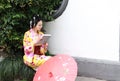 Traditional Asian Japanese beautiful Geisha woman wears kimono hold a umbrella reading book in a summer nature