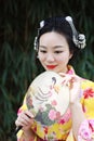 Traditional Asian Japanese beautiful woman with a fan on hand stand by bamboo in a garden
