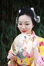 Traditional Asian Japanese beautiful woman with a fan on hand stand by bamboo in a garden Royalty Free Stock Photo