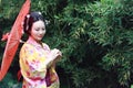 Traditional Asian Japanese bride with kimono hold a red umbrella stand by bamboo in a park