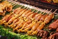 Traditional Asian Thai street food and fast food, delicious grilled squid calamari skewers in food market stall background.