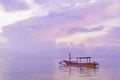 Traditional Balinese wooden fishing boat at dawn on Sanur beach in Bali. Cloudy pink dawn sky. Reflection in the water. Royalty Free Stock Photo