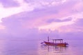 Traditional Balinese wooden fishing boat at dawn on Sanur beach in Bali. Cloudy pink dawn sky. Reflection in the water.