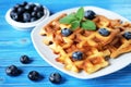 Traditional belgian waffles with fresh berrys and sugar powder on white plate, blue wooden background. Royalty Free Stock Photo