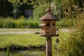 traditional birdhouse with water and seed feeders on a wooden post