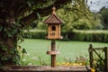 traditional birdhouse with water and seed feeders on a wooden post