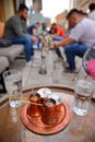 Traditional Bosnian coffee cups with a copper tray with young people smoking Shisha or Hookah in the background,