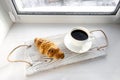 Coffee and croissant on a tray on the windowsill. Traditional breakfast.