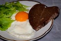 Traditional breakfast with fried egg protein and yolk, slices of heard-shaped bread and greenery Royalty Free Stock Photo