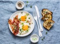 Traditional breakfast or snack - fried eggs, bacon, grilled bread on blue background, top view.