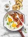 Traditional breakfast or snack - fried eggs, bacon, grilled bread on light background, top view