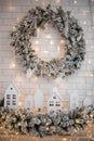 A traditional bright Christmas wreath hanging over the fireplace, on a white brick wall, and decor small houses on a Royalty Free Stock Photo