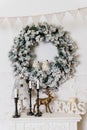 A traditional bright Christmas wreath hanging over the fireplace, on a white brick wall, home decor for winter holidays Royalty Free Stock Photo